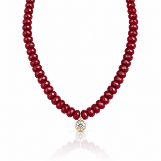 Close-up of faceted red gemstone beads and round clear cubic zirconia pendant in an 18K gold-plated setting.