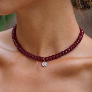 Model wearing an adjustable red faceted gemstone necklace with round CZ pendant and brown cord.