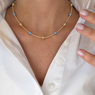 Model wearing a 14K gold-filled beaded necklace with light blue cubic zirconia ball accents and polished gold beads.
