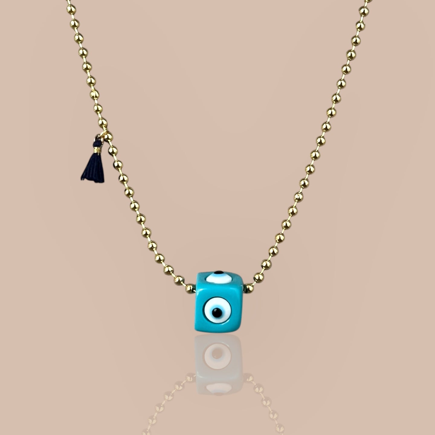 Gold ball chain necklace with turquoise cube pendant featuring an evil eye symbol, representing protection and elegance.