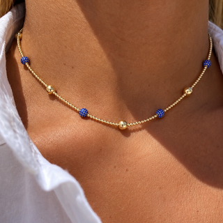 Model wearing a 14K gold-filled beaded necklace with blue cubic zirconia ball accents and polished gold spheres.